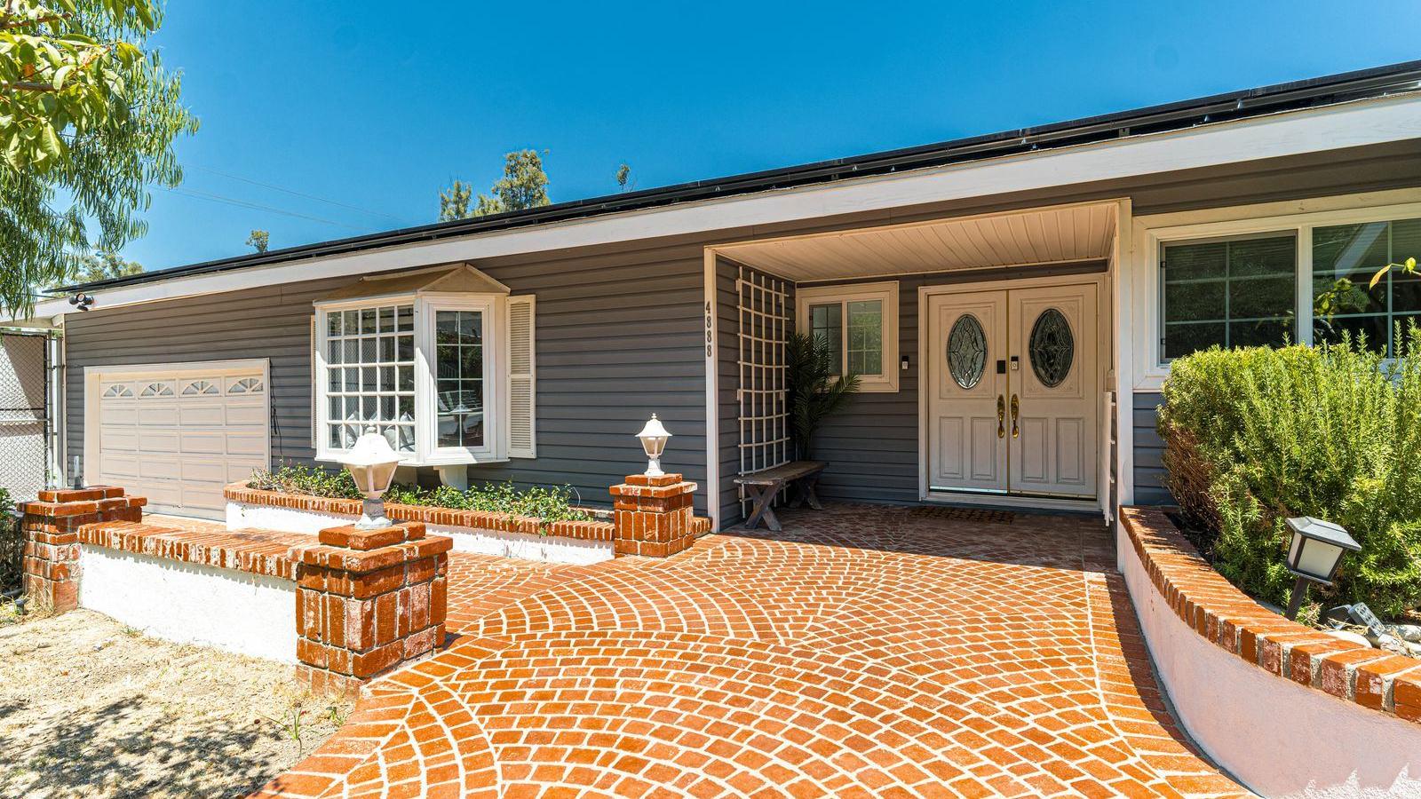 Single-story home with a curved red paver driveway and entry patio