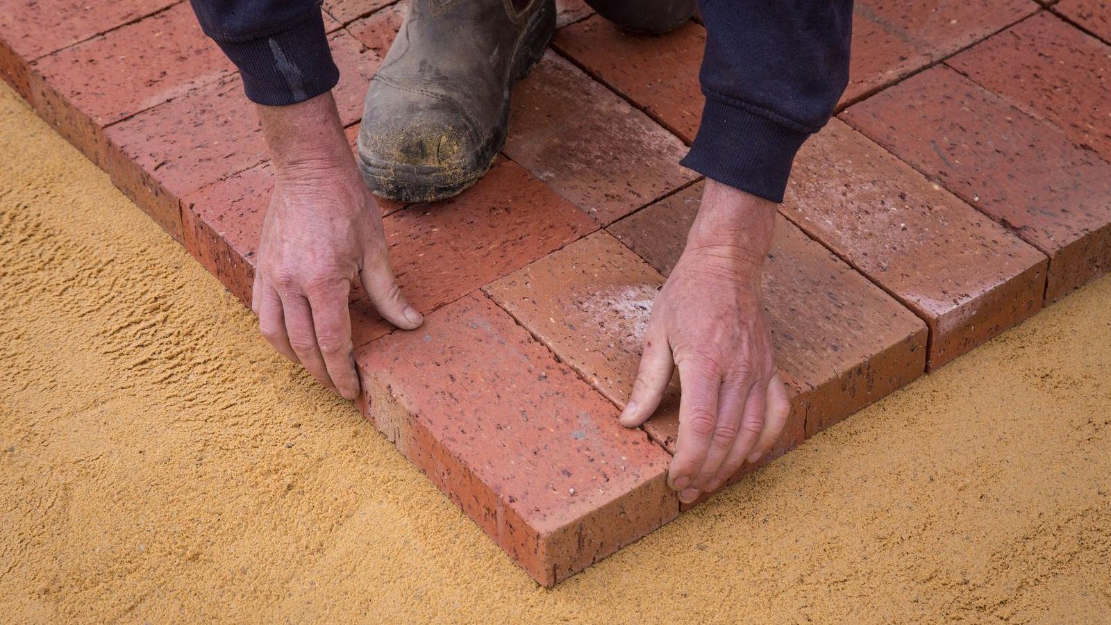 Installer setting pavers by hand on a leveled sand bedding layer