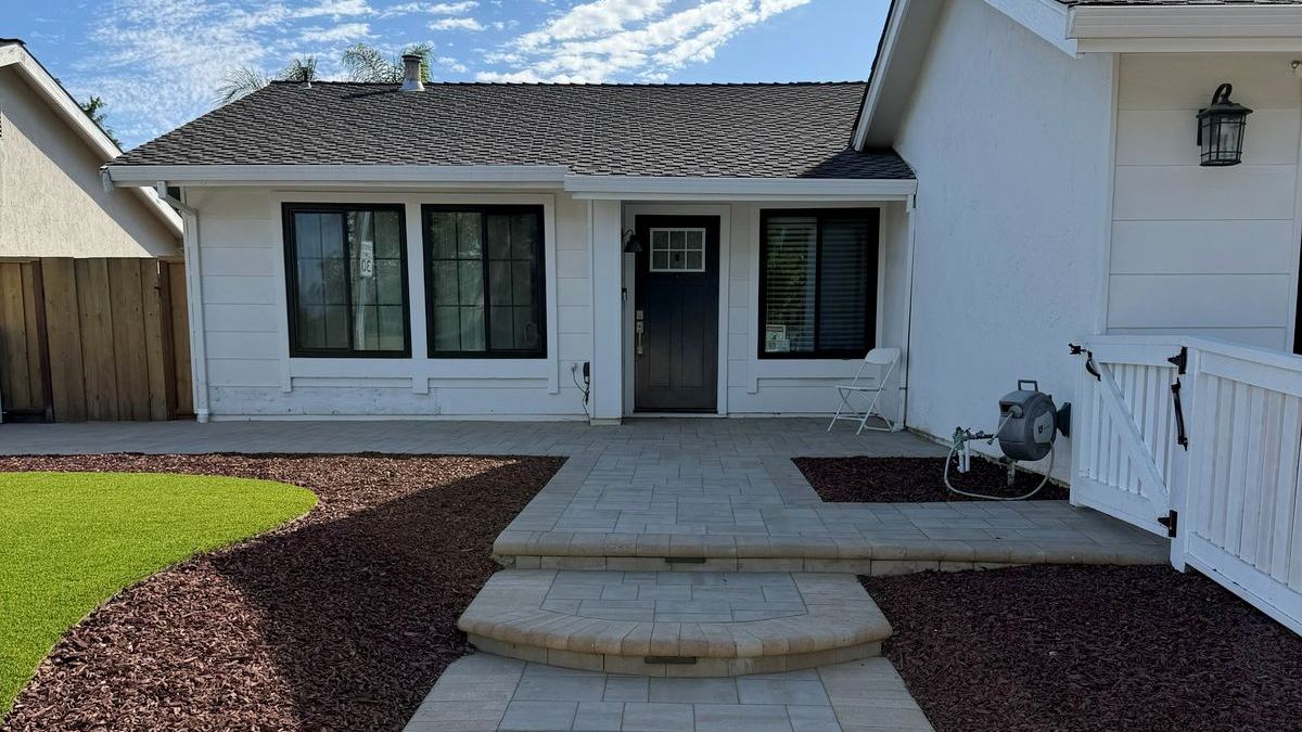 Curved paver steps and a walkway leading to a front door, with red mulch and an artificial turf island