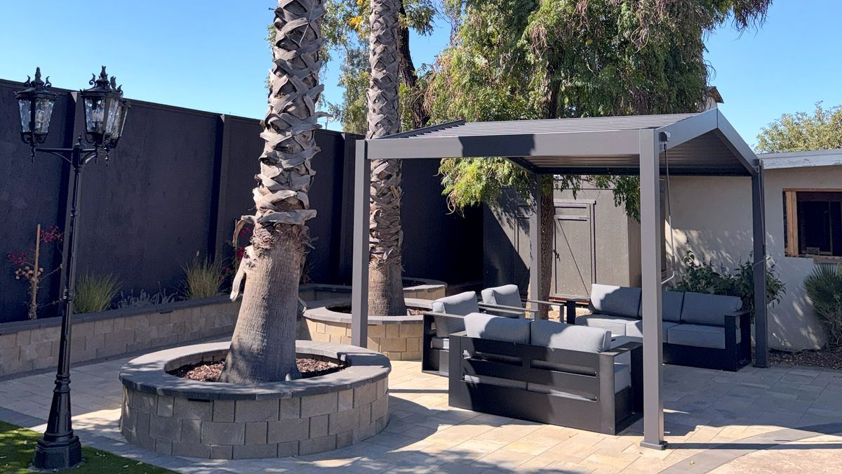 Paver patio with a round stone seat wall around a palm tree and a louvered pergola over a lounge