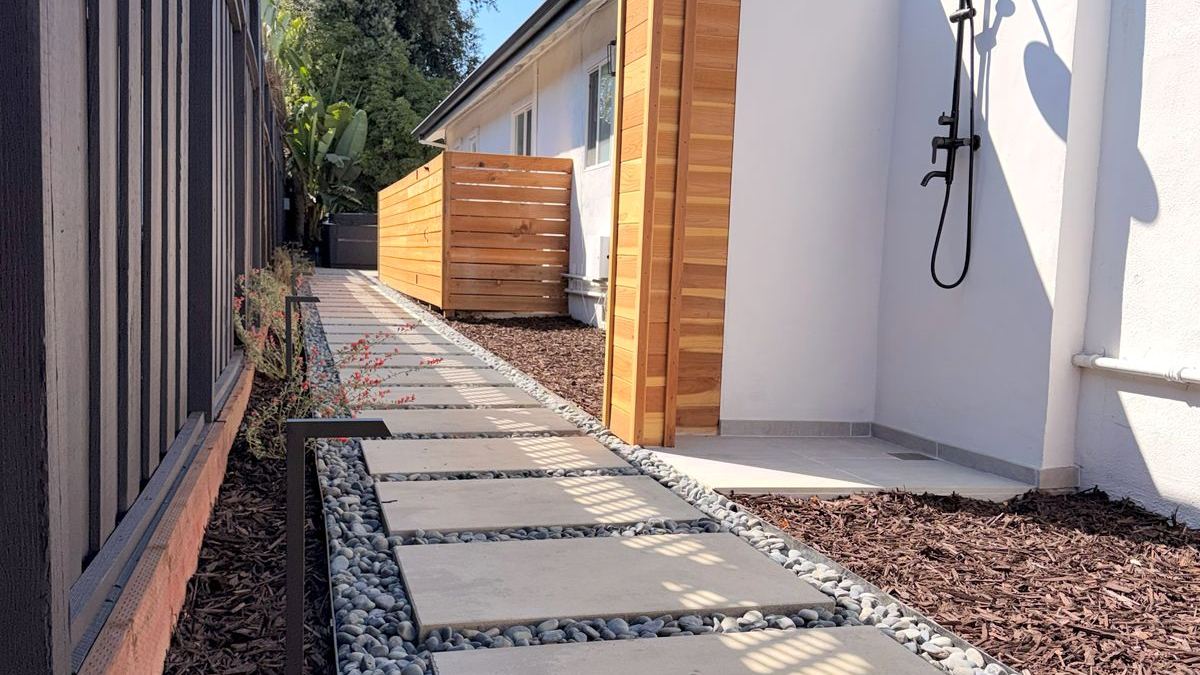 Side-yard walkway of large stepping stones with pebble borders, a cedar privacy screen and an outdoor shower
