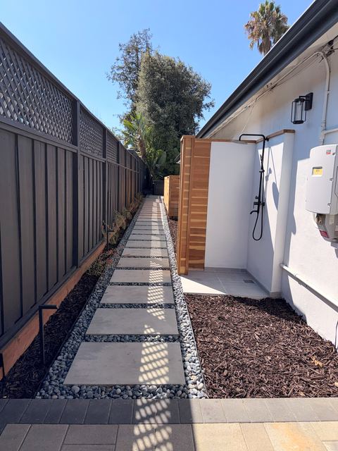 Side-yard walkway of large stepping-stone pavers with pebble borders and an outdoor shower