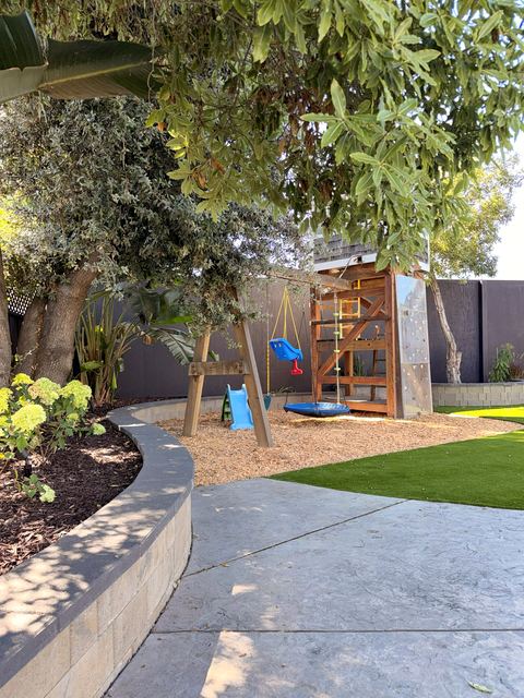 Curved planter wall and concrete path leading to the play area and artificial turf
