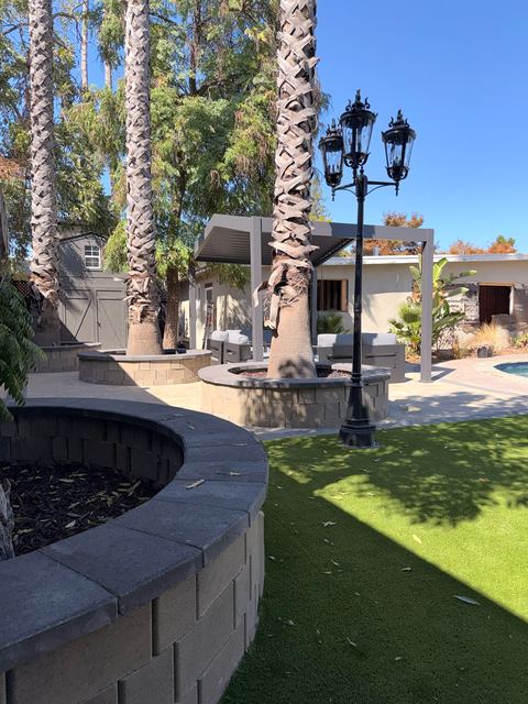 Lamp posts beside a curved stone wall and artificial turf, with a pergola in the background