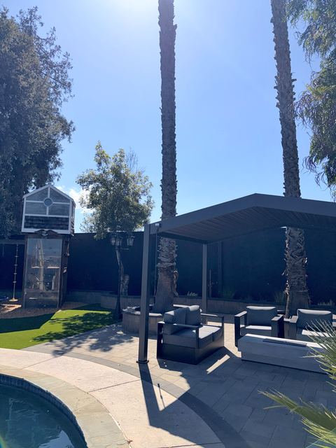 Louvered pergola with lounge chairs next to the pool, with palm trees behind