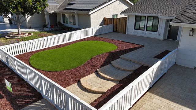 A finished paver patio with steps, artificial turf and a white fence at one of our San Jose projects