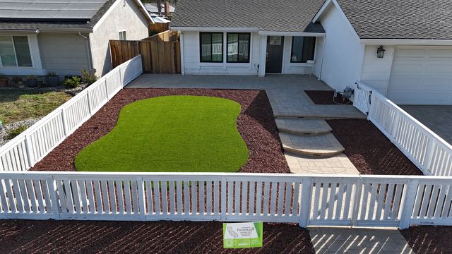 White picket fence around a front yard with artificial turf, red mulch and curved paver steps in front of the house