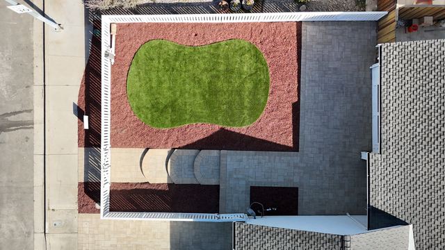 Top-down view of the front yard: an artificial turf island in red mulch inside a white picket fence