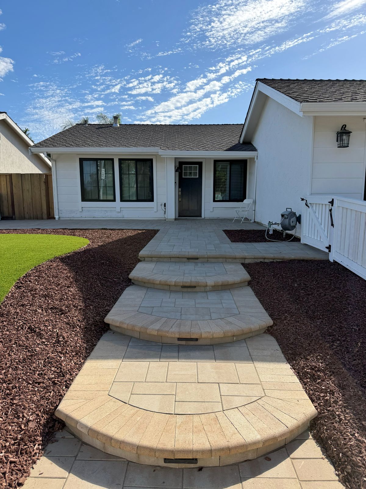 Curved paver steps leading to the front door of a white house, with red mulch and artificial turf on each side