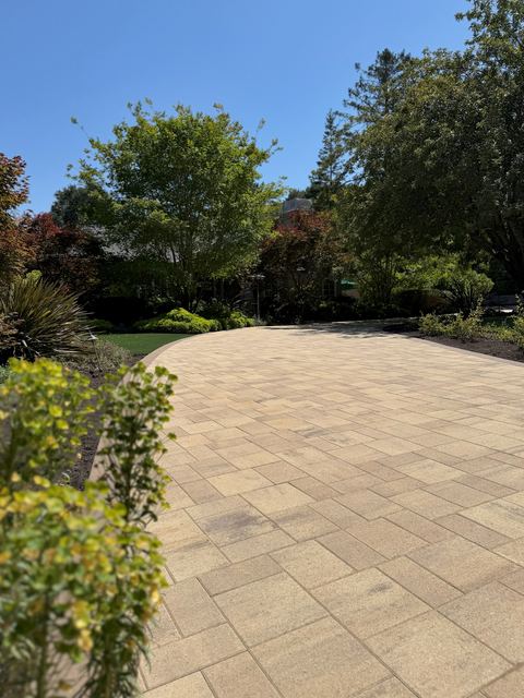 Curved paver driveway sweeping past planting beds and mature trees