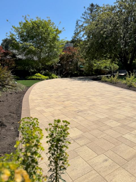 Curved paver driveway with a stone edge border beside planting beds