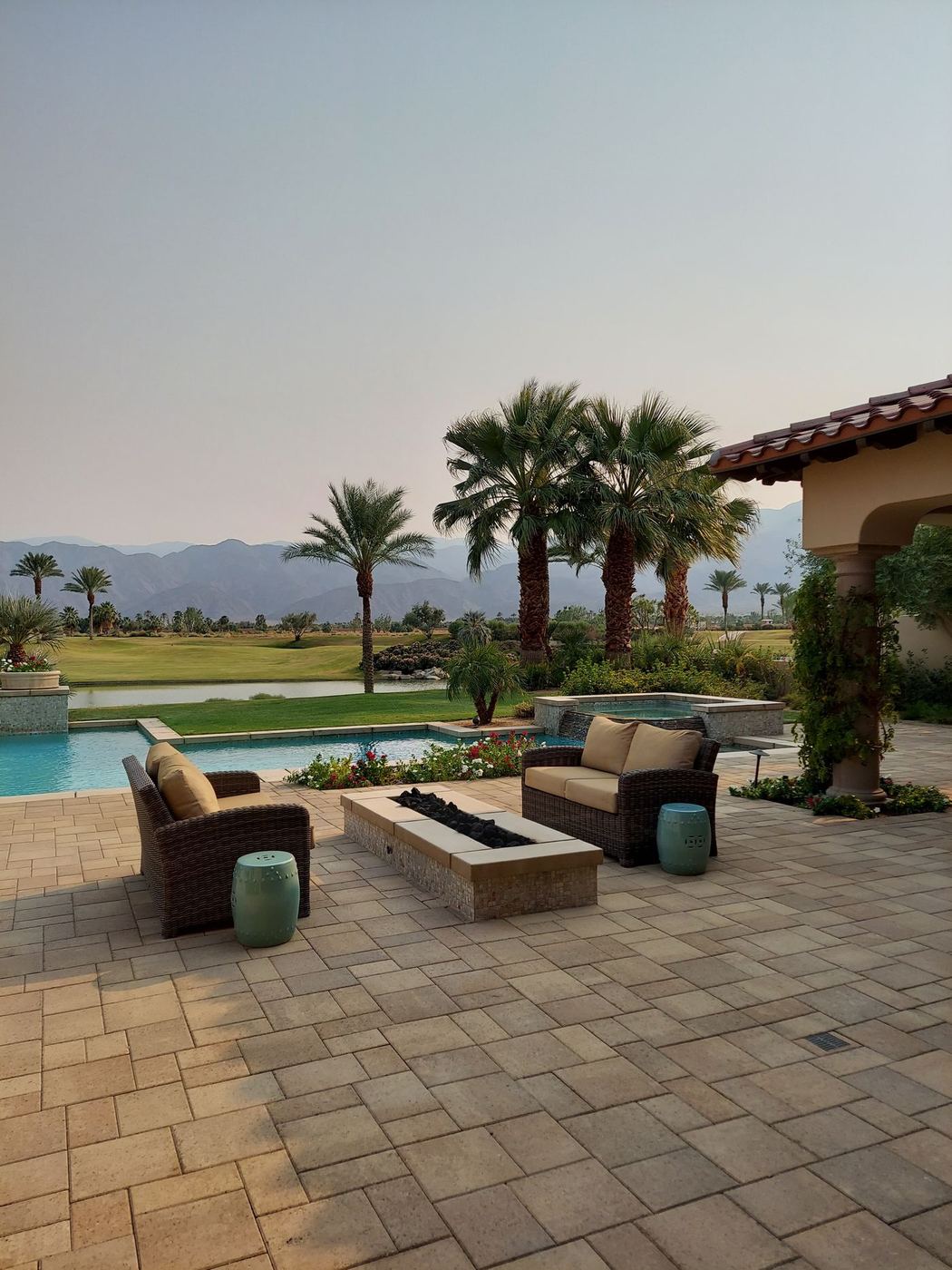 Paver patio with a gas fire table, lounge seating and palm trees beside a pool