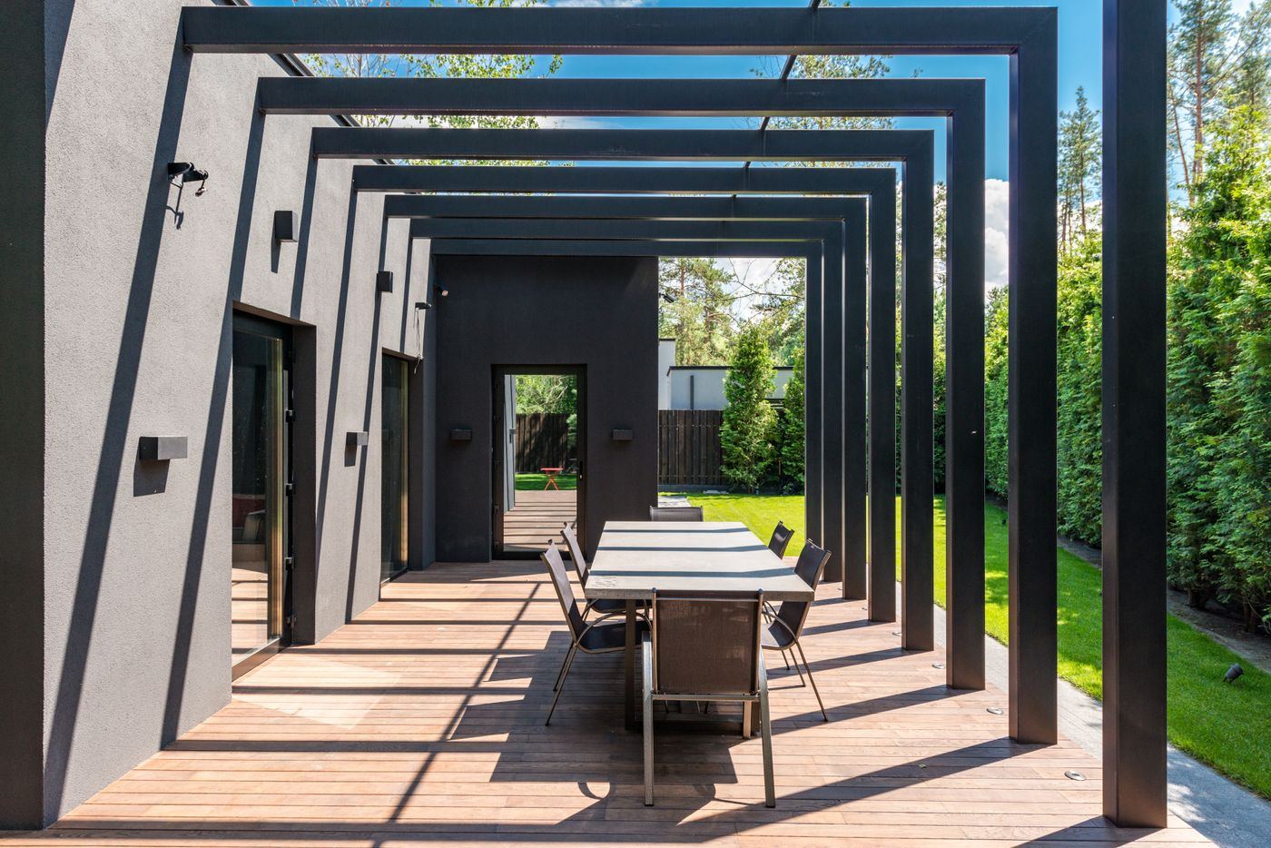 Modern black steel pergola over a wood deck with a long dining table